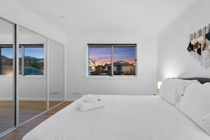 Un dormitorio con una cama grande, vistas a un atardecer a través de una ventana y un ventanal corredero que da a un balcón.