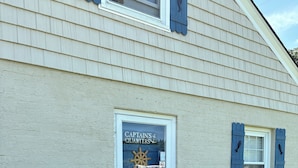A building with a white exterior, a glass door with a sign reading "Captains & Quarters," and a small garden area with a wooden post and a potted plant. - Charming, nautical themed 1-bedroom upstairs apartment in Washington ,NC (Washington)