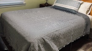 A bedroom with a bed, a nightstand, a lamp, a window with blinds, and wall art. - Charming, nautical themed 1-bedroom upstairs apartment in Washington ,NC (Washington)