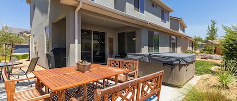A two-story house with a covered patio area featuring a wooden table and chairs.