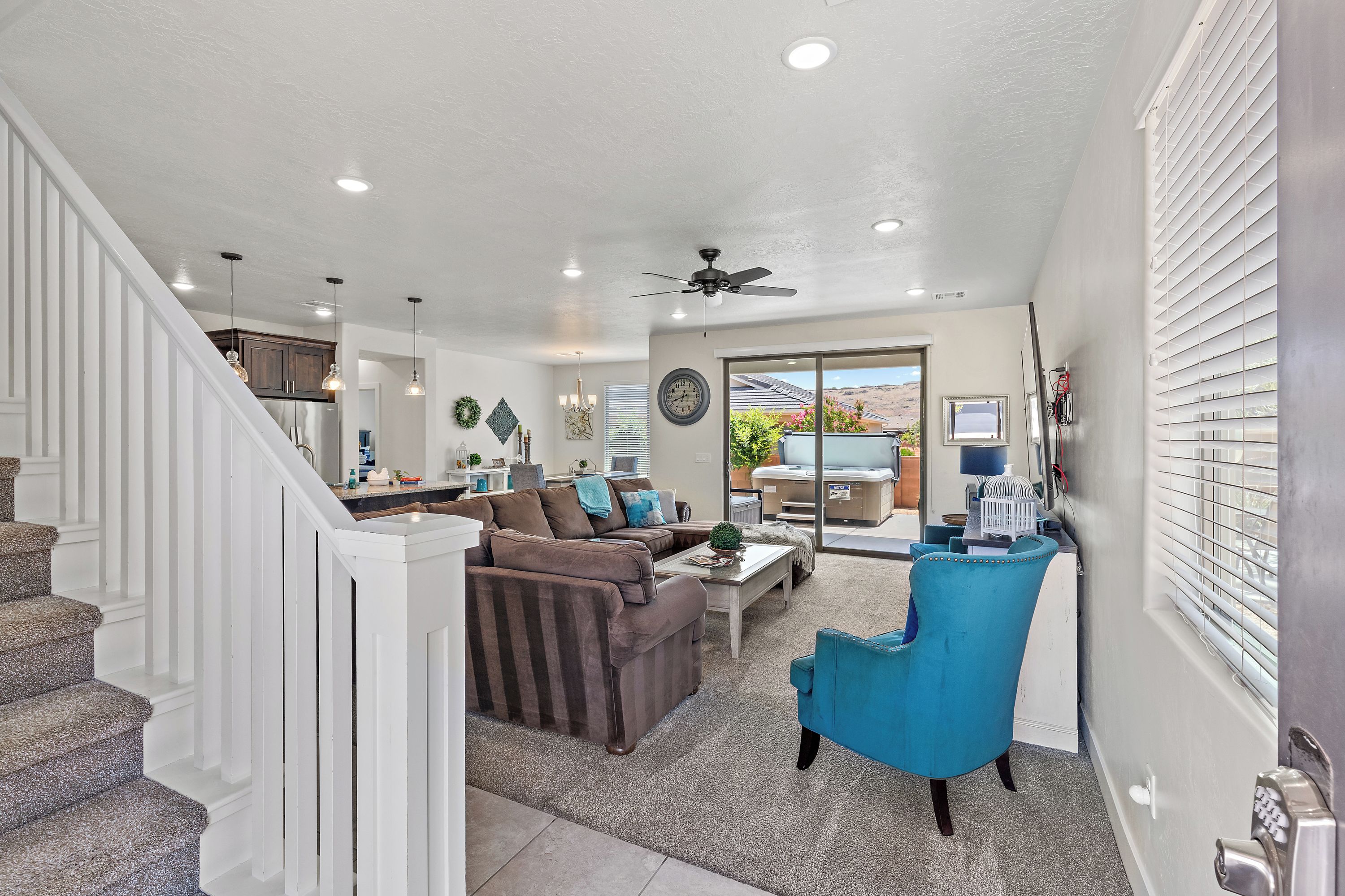 A spacious living area with a staircase, a ceiling fan, and a view through a glass door to the outside.