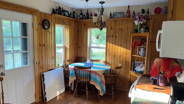 A wooden interior with a dining table, chairs, a ceiling fan, and a kitchen area with a refrigerator and coffee maker.