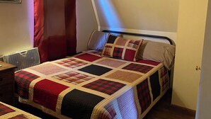A bedroom with a bed, a chair, a heater, and a ceiling fan.
