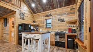 A cabin interior with a wooden interior, a kitchen area with a stove, oven, and sink, and a bar area with stools. - Cozy Cabin 3 miles to WPG Slps 4, ATV friendly (Mena)