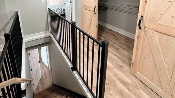 Una scala con finiture in legno e ringhiere nere, che conduce a una stanza con un'ampia porta in legno e un soffitto bianco.