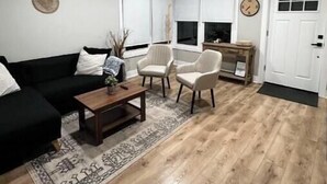 Un soggiorno con un divano nero, due poltrone bianche, un tavolino in legno e un tappeto decorato.