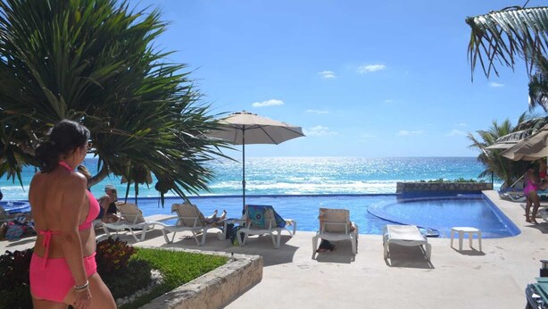 A poolside area with lounge chairs, a swimming pool, and a view of the ocean. - CANCUN OCEANFRONT STUDIO SUNFLOWER CONDOMINIUM (Cancun)
