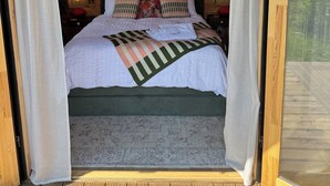 Un dormitorio acogedor con techo de madera, cama con cabecera verde y vistas a la vegetación.