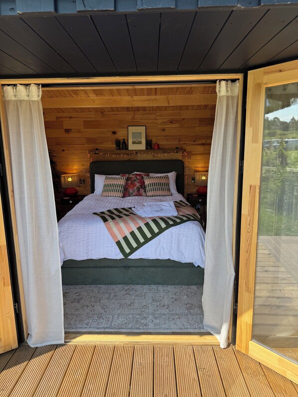 Une chambre confortable avec un plafond en bois, un lit doté d’une tête de lit verte et une vue sur la verdure environnante.
