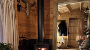 A cozy room with a wood-burning stove, wooden walls, a sign reading "Friends Gather Here", and a door leading to another area.