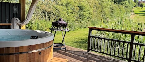 A wooden deck with a hot tub, outdoor seating, and a view of a green landscape.