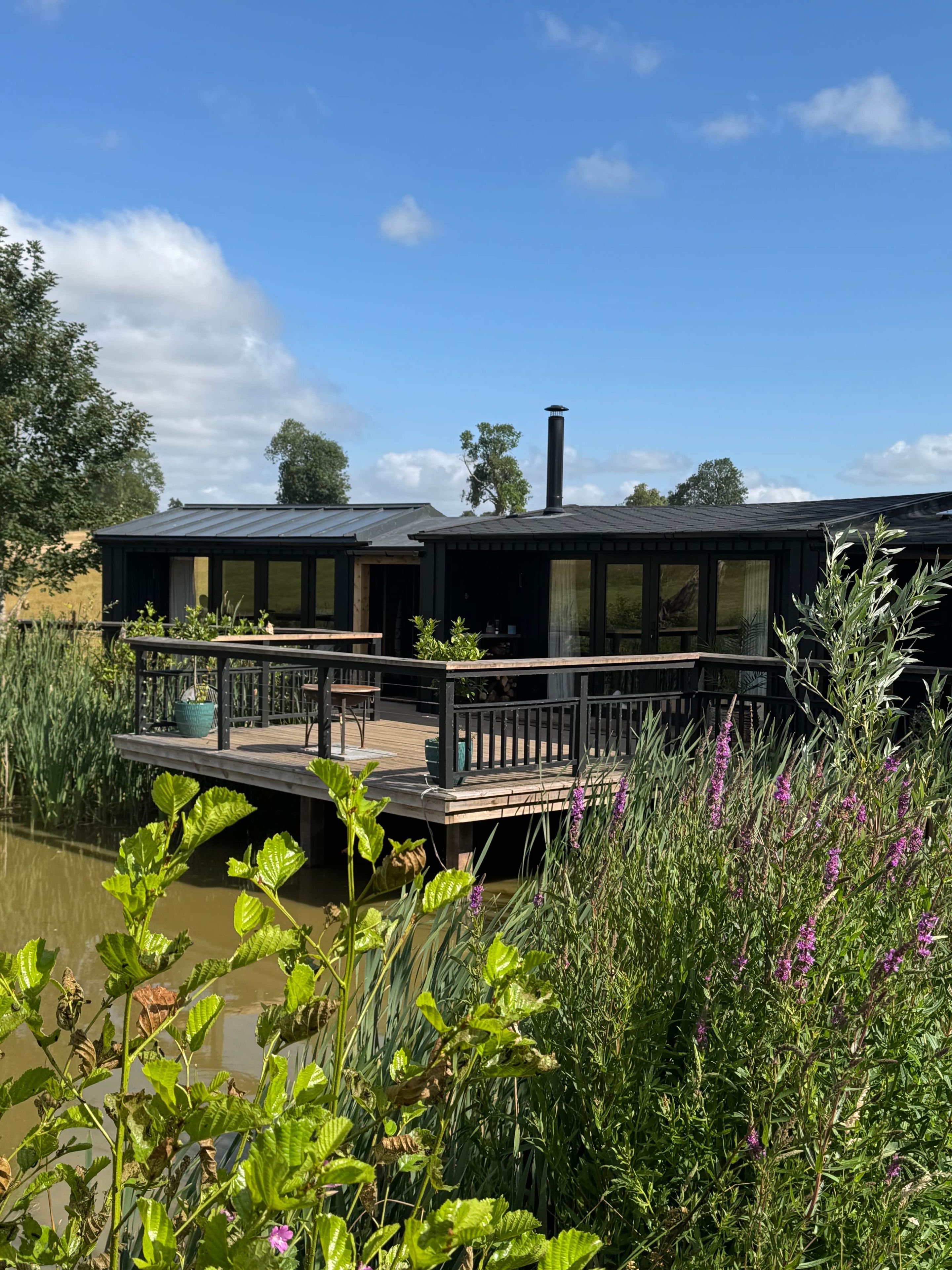 A houseboat with a deck and a chimney, surrounded by water and vegetation.