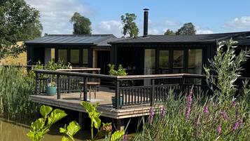 A houseboat with a deck and a chimney, surrounded by water and vegetation.