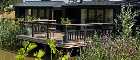 A houseboat with a deck and a chimney, surrounded by water and vegetation.