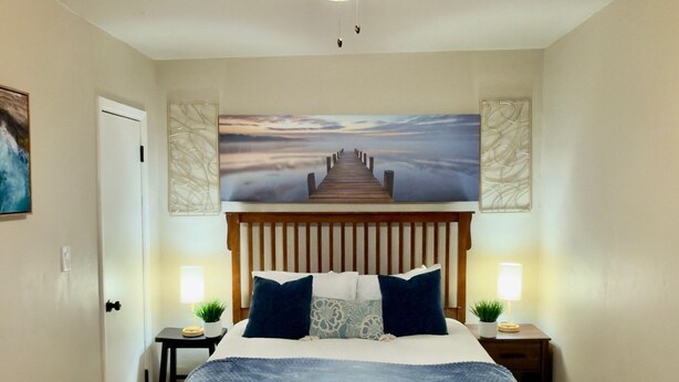 Ein Schlafzimmer mit einem hölzernen Bett, einem Deckenventilator, einem Gemälde eines Piers und zwei Nachttischlampen.