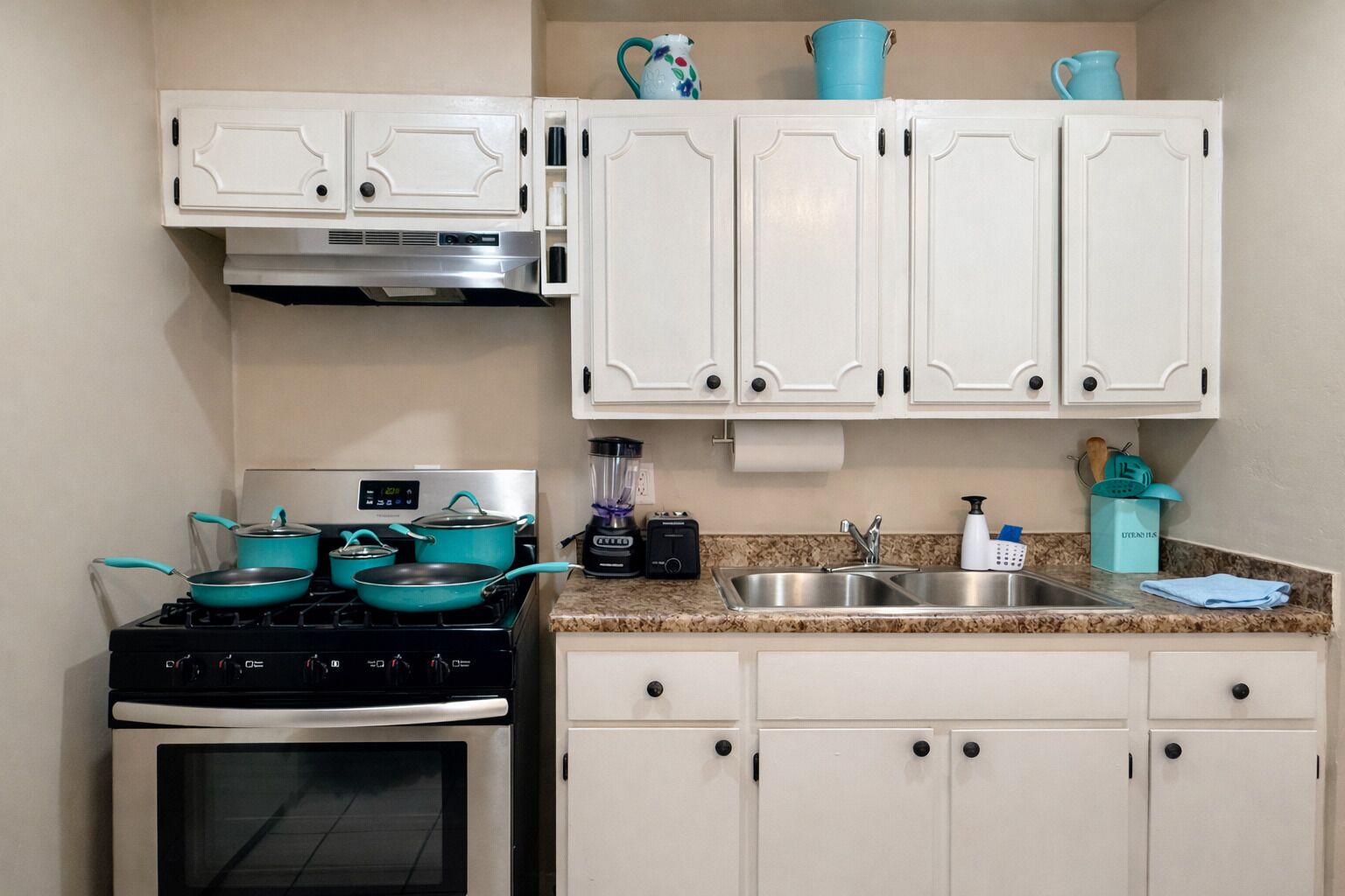 Une cuisine avec des armoires blanches, une cuisinière, un évier et des ustensiles de cuisine de couleur turquoise.