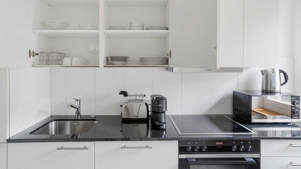 A modern kitchen with white cabinetry, a black countertop, a Bosch induction cooktop, a coffee maker, and a toaster. - Blueground | Basel-Iselin, balcony, nr Rhine (Basel)