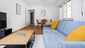 A modern living room with a sofa, coffee table, and TV. There is a dining area with chairs and a table. - Blueground | Basel-Iselin, balcony, nr Rhine (Basel)