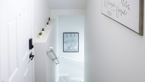 A white interior hallway with a door, a handrail, a framed welcome sign, and a patterned wall art piece. - Charming 2-bedroom house in delightful Calgary with WiFi (Calgary)