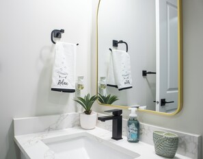 Un baño moderno con un lavamanos de mármol, una planta en maceta, un dispensador de jabón y dos toallas colgadas de ganchos.
