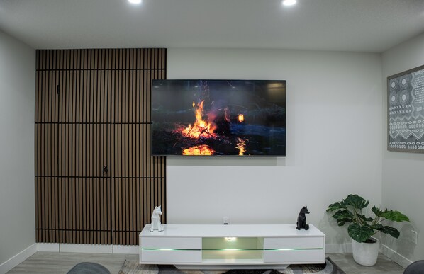 Una sala de estar moderna con un televisor de pantalla plana montado en la pared, un mueble blanco de entretenimiento debajo y una planta grande en maceta a la derecha.