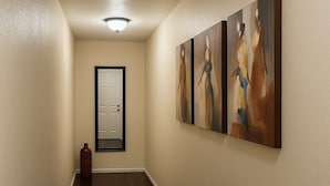 A hallway with dark wooden flooring, beige walls, and three abstract paintings on the right wall. - Wynwood Hostel (Miami)