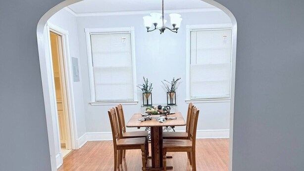Una sala da pranzo con un tavolo e sedie in legno, un lampadario e due finestre con persiane.
