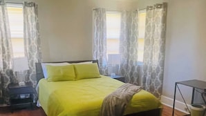 Una camera da letto con un letto, tende, un comodino, un tavolino e un pavimento in legno.
