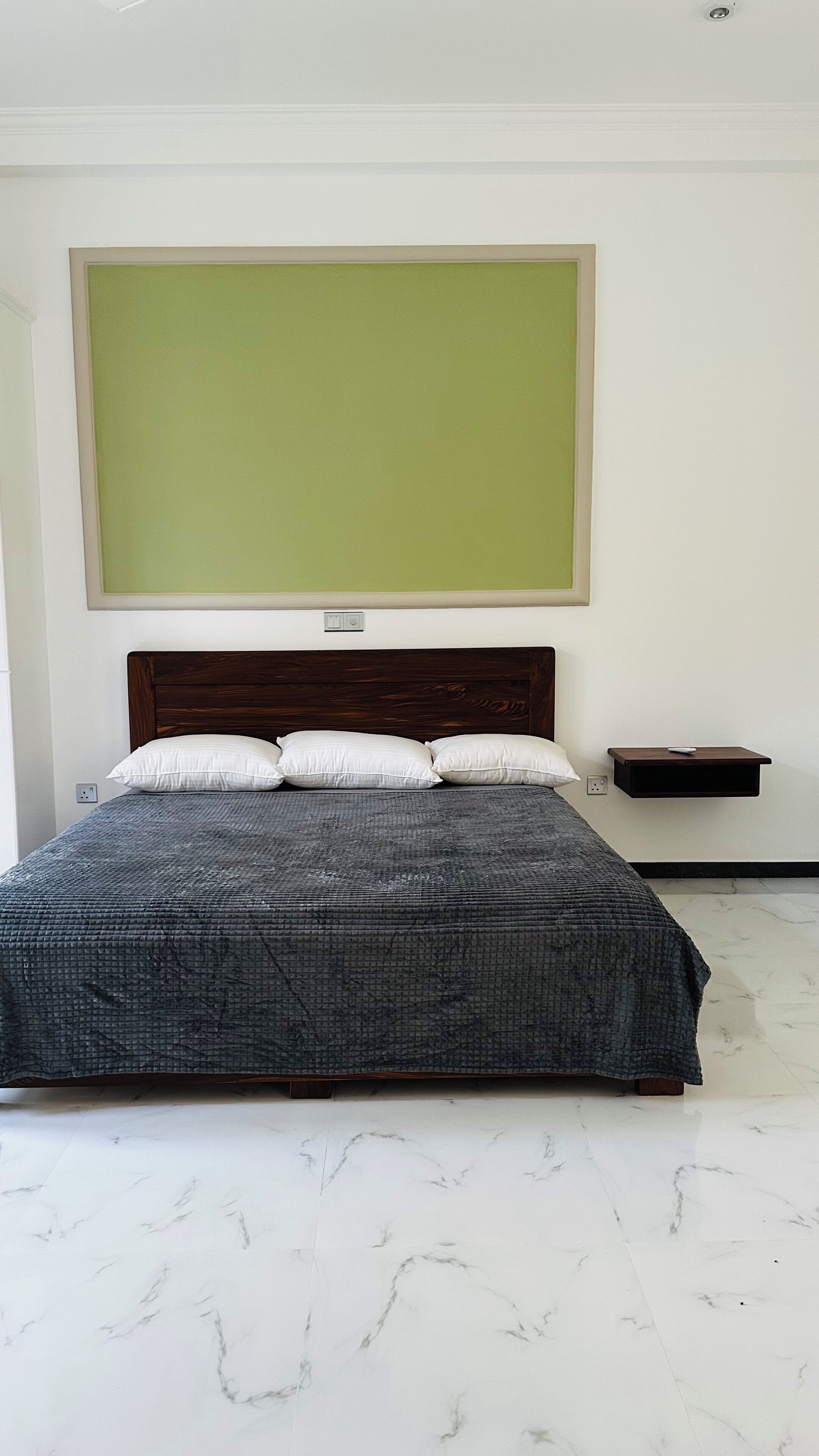 Une chambre à coucher avec un grand lit, une tête de lit en bois, une table de chevet et un mur vert au-dessus du lit.