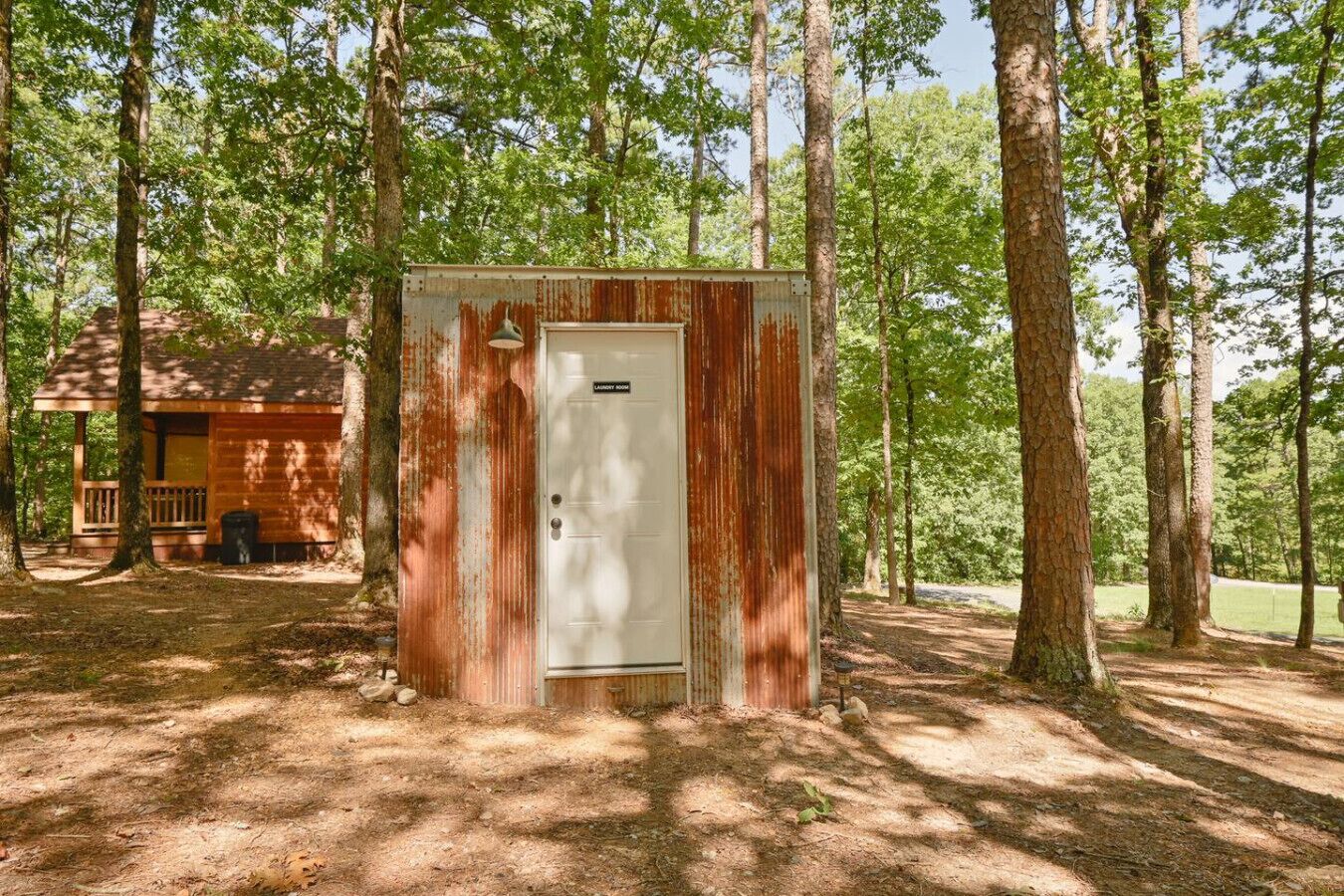 A rustic wooden cabin with a metal utility shed labeled "Laundry Room" in a wooded area.