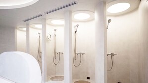 A modern bathroom with three separate shower stalls, each with a round sink and overhead lighting.