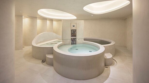 A modern spa with three hot tubs arranged in a semi-circle, a central water feature, and recessed lighting.