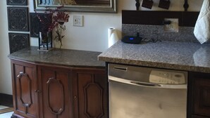 A compact kitchen with a built-in dishwasher, a mirror above the counter, and a decorative metal rack with hanging items. - Furnished bedroom, bathroom, kitchen in a guard-gated community (Bell Canyon)