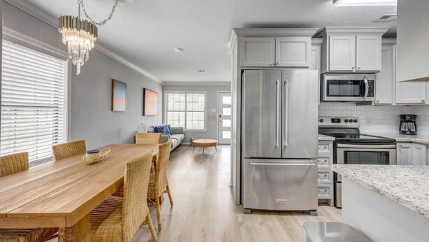 A modern kitchen with stainless steel appliances, a dining area with a wooden table and wicker chairs, and a chandelier. - New Listing!  Breezy Palms (Aransas Pass)