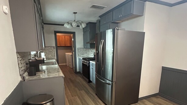 A modern kitchen with a stainless steel refrigerator, wooden flooring, and a trash can. - Desert Oasis w/ Heated Pool, Fire Pit & Family Fun (Odessa)