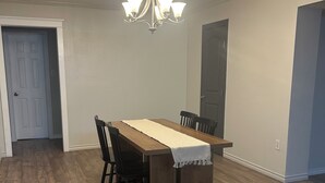 A dining area with a wooden table and chairs, a chandelier, and a white door in the background. - Desert Oasis w/ Heated Pool, Fire Pit & Family Fun (Odessa)