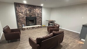 A spacious living room with a stone fireplace, leather sofas, and a foosball table. - Desert Oasis w/ Heated Pool, Fire Pit & Family Fun (Odessa)