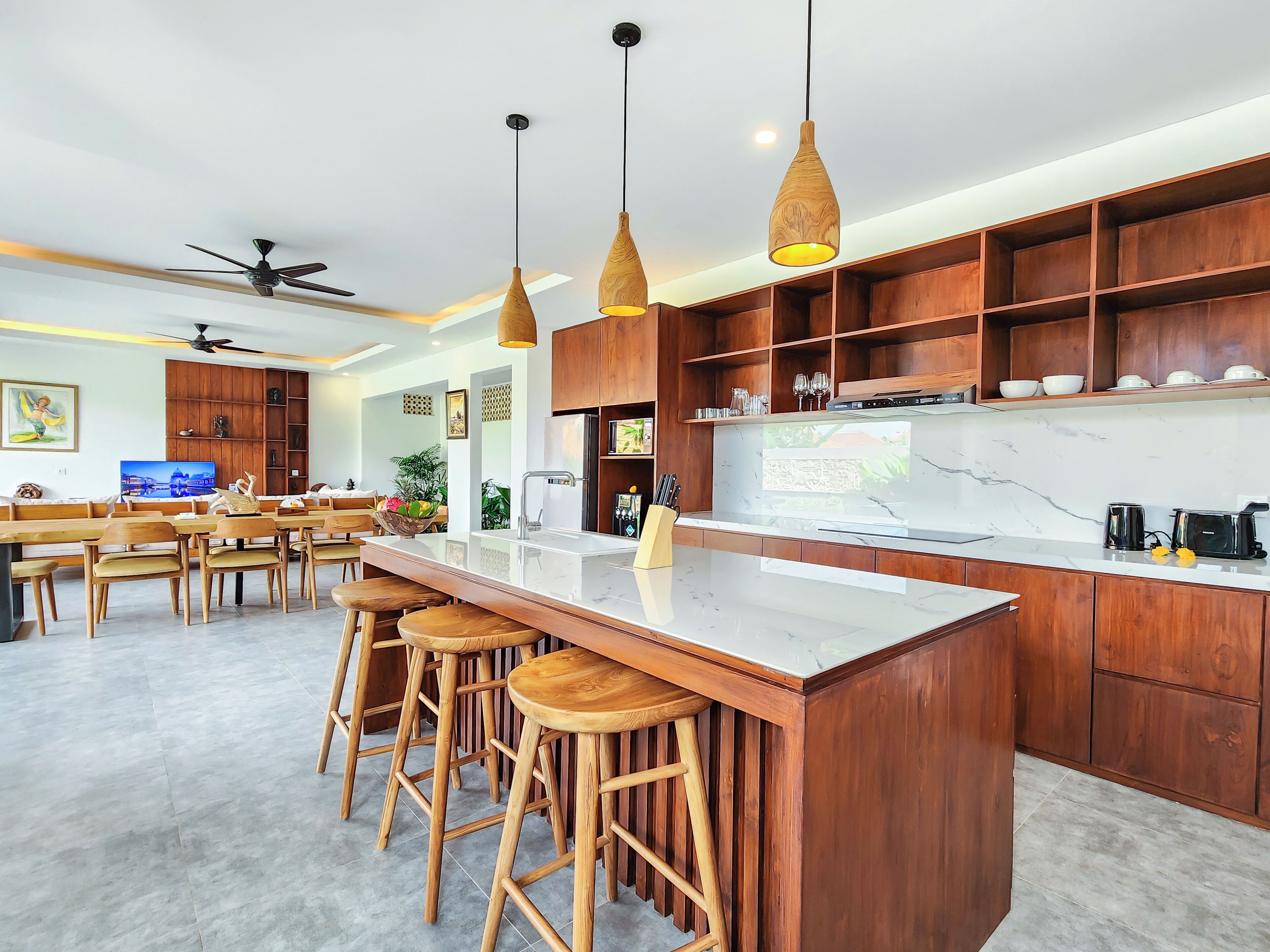 A modern kitchen with wooden cabinetry, a marble countertop, and a bar area with stools.
