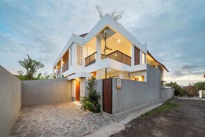 A modern two-story villa with a balcony, a covered entrance, and a stone-paved driveway.