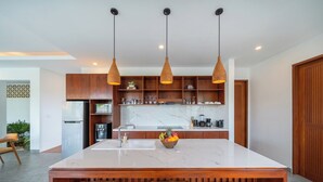 A modern kitchen with a central island, wooden bar stools, pendant lighting, and a marble countertop.