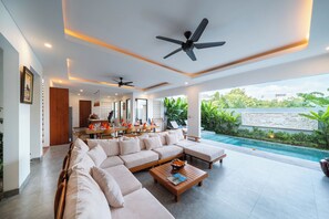 A spacious living area with a large sofa, a coffee table, and a poolside view.