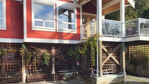 A two-story building with a red exterior and white trim, featuring large windows and a balcony. - Cozy Pender Island Cottage (Pender Island)