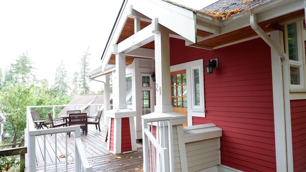 A red house with a white porch and a wooden deck. - Cozy Pender Island Cottage (Pender Island)