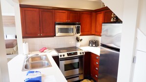 A compact kitchen with wooden cabinets, stainless steel appliances, a built-in microwave, a toaster, and a sink. - Cozy Pender Island Cottage (Pender Island)