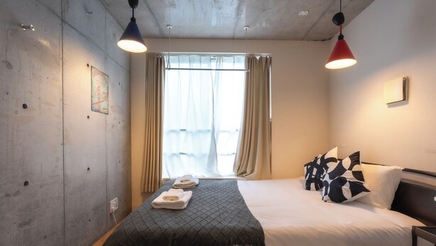 Una habitación de hotel con cama, ventana con cortinas, lámpara de pared y un adorno en la pared.