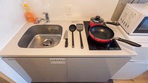 Una cocina con un lavamanos, una placa de inducción roja, un microondas y diferentes utensilios.