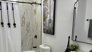 A modern bathroom with a marble floor, a bathtub, a toilet, a sink with a mirror, and a shower curtain.