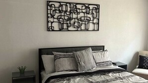 A modern bedroom with a bed, a bedside table with a plant, a wall art piece, and a chair.