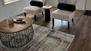 A room with two striped armchairs, a round coffee table, and a small side table. There is a potted plant in the corner and a door with a light switch.