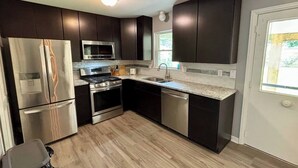 A modern kitchen with dark cabinets, stainless steel appliances, and a granite countertop. - 2 King Bedroom Ranch - Hot Tub -Pets and Kids Welcome - Fenced Yard - Smart TV (Gahanna)